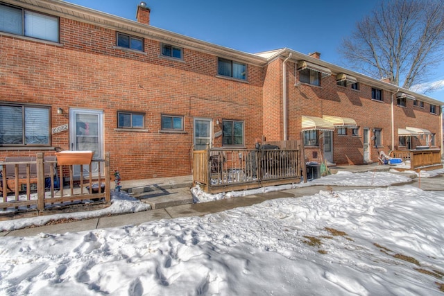 snow covered property with a chimney, central AC, and brick siding