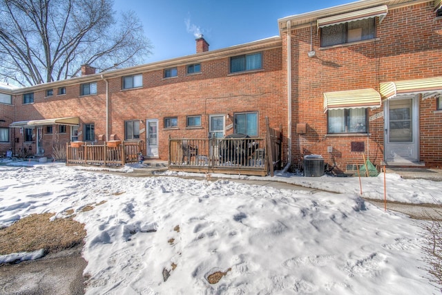 snow covered rear of property with a wooden deck, a chimney, and brick siding