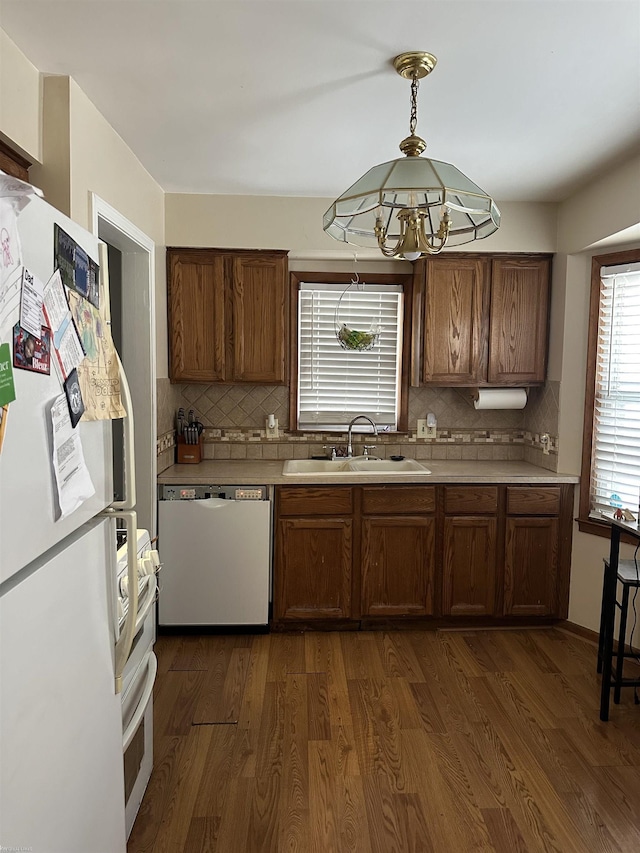 kitchen with white appliances, dark wood-type flooring, a sink, hanging light fixtures, and light countertops