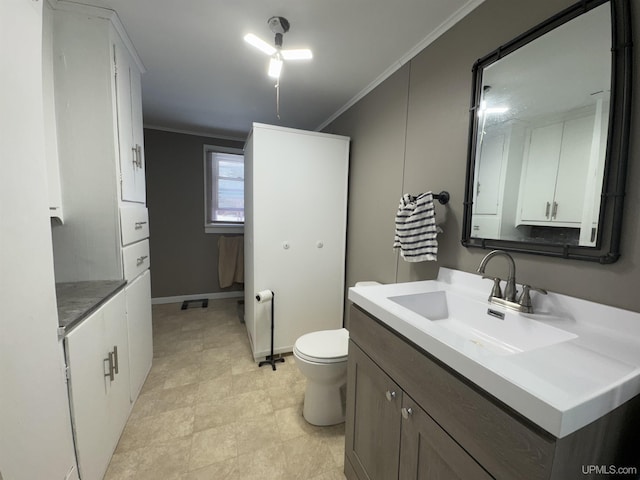 bathroom with toilet, baseboards, vanity, and crown molding