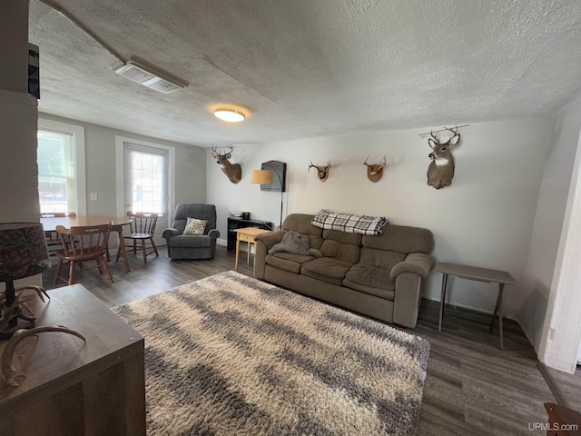 living area with dark wood-style floors, a textured ceiling, visible vents, and baseboards