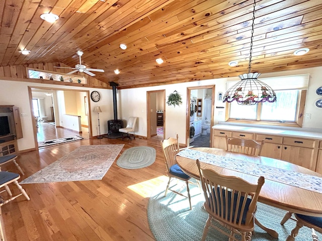 dining area with a wood stove, light wood-style floors, wood ceiling, and vaulted ceiling