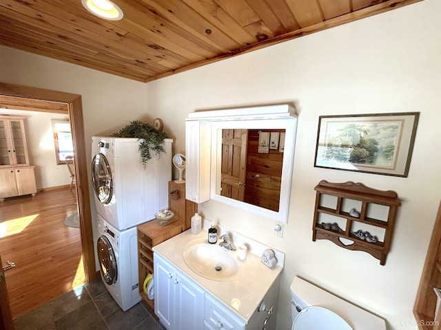 bathroom with stacked washer and dryer, toilet, wood ceiling, tile patterned floors, and vanity