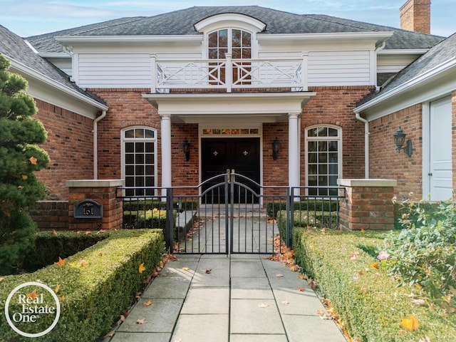 doorway to property with brick siding, a gate, a balcony, and fence