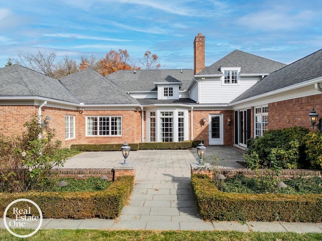 rear view of house featuring brick siding, a chimney, a patio area, and a shingled roof