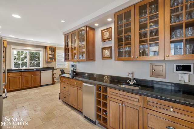 kitchen with a sink, stainless steel dishwasher, brown cabinets, dark stone countertops, and glass insert cabinets