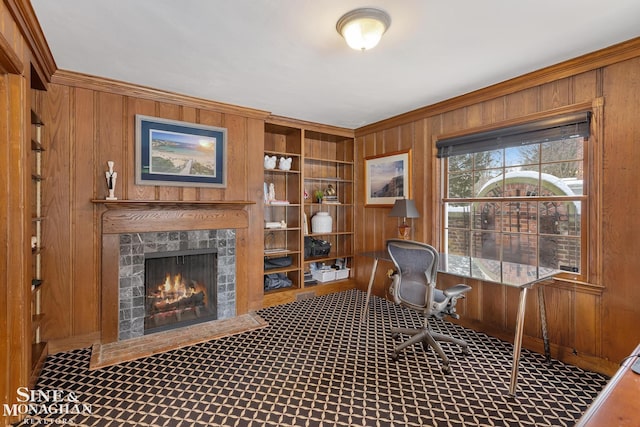 office area with a warm lit fireplace, built in shelves, crown molding, and wooden walls