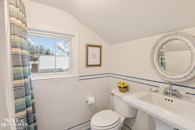 bathroom featuring vaulted ceiling, toilet, a sink, and tile walls