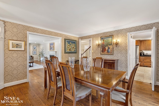 dining area featuring crown molding, light wood finished floors, a fireplace, and wallpapered walls