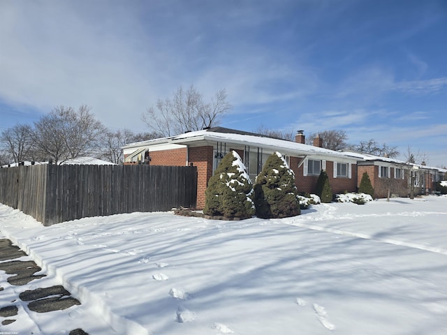 snow covered property with brick siding, a chimney, and fence