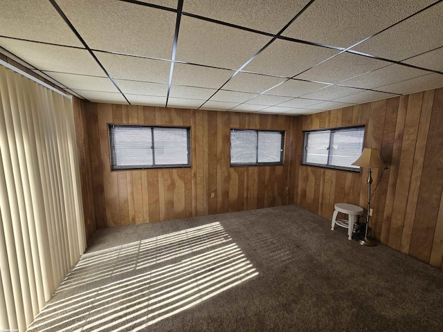 carpeted empty room with a paneled ceiling and wood walls