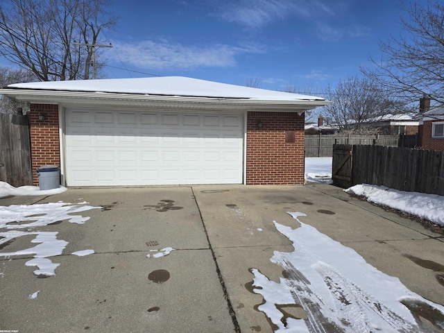 snow covered garage featuring fence and a detached garage