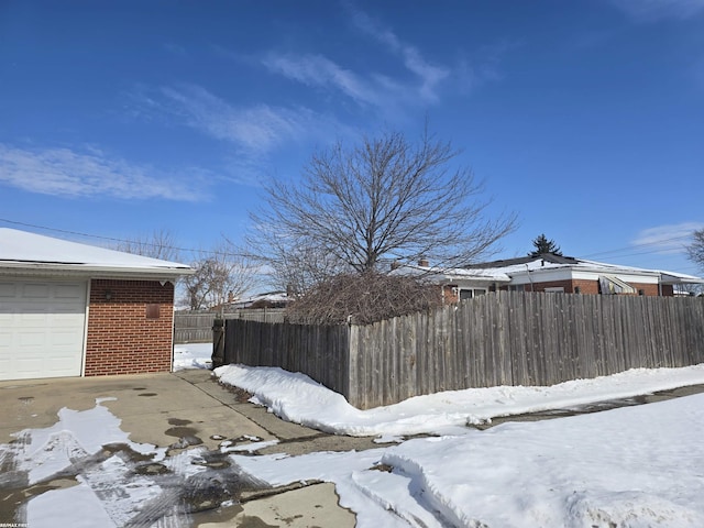 yard layered in snow featuring a garage and fence