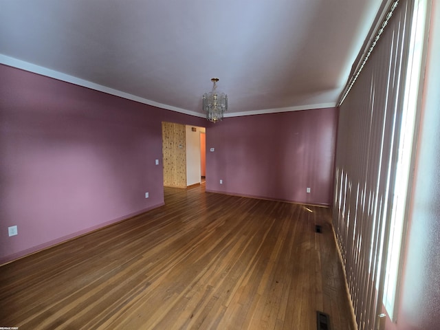 empty room featuring baseboards, a chandelier, dark wood finished floors, and crown molding