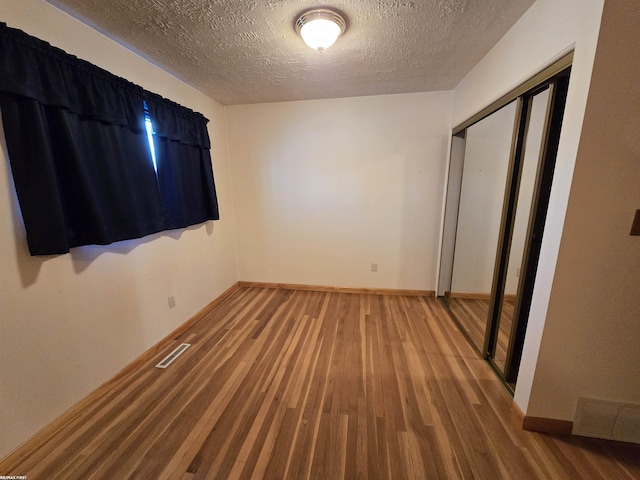 unfurnished bedroom with baseboards, a closet, visible vents, and wood finished floors