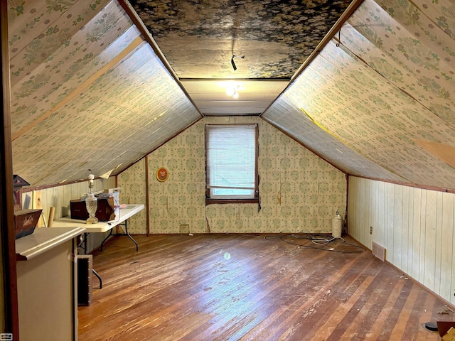 additional living space with lofted ceiling, wooden walls, visible vents, and wood finished floors