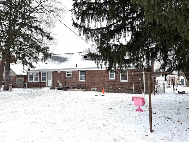 snow covered back of property with entry steps, fence, and brick siding