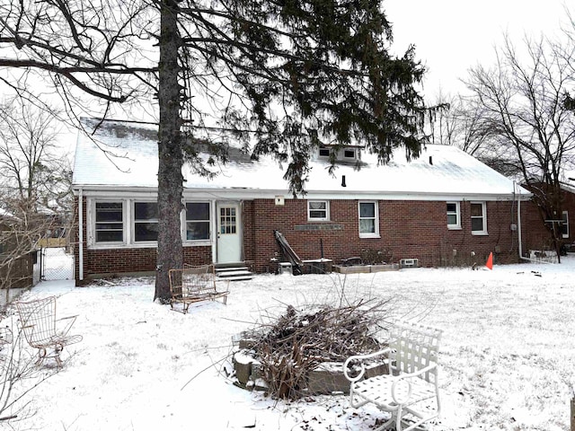 snow covered rear of property with entry steps and brick siding