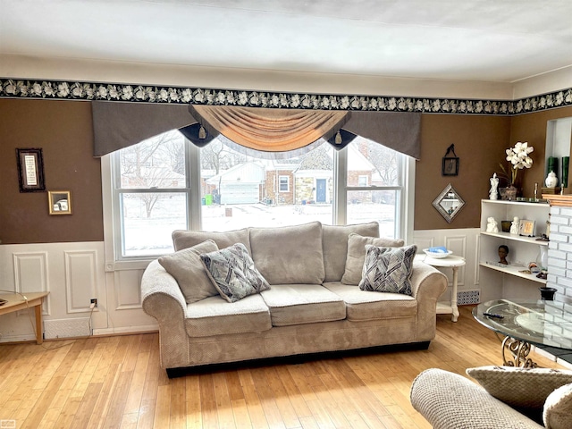 living room with a wainscoted wall, light wood finished floors, and a decorative wall