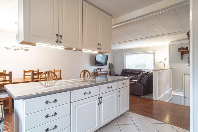 kitchen with open floor plan, beamed ceiling, light countertops, white cabinetry, and light tile patterned flooring