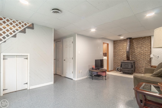 finished below grade area with a wood stove, visible vents, baseboards, and a drop ceiling