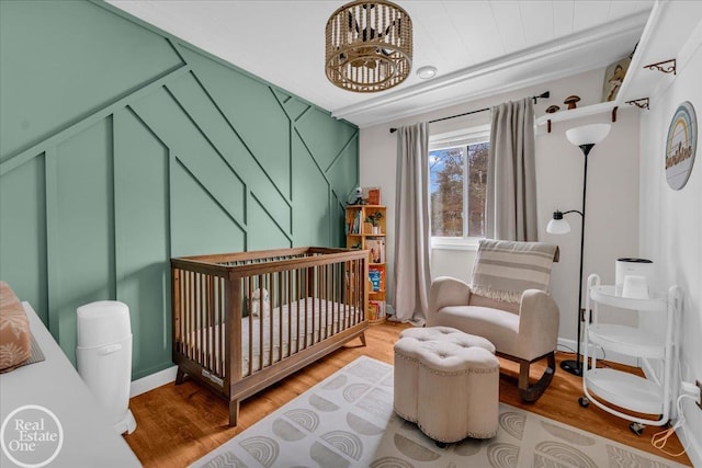 bedroom featuring a nursery area, wood finished floors, and an inviting chandelier