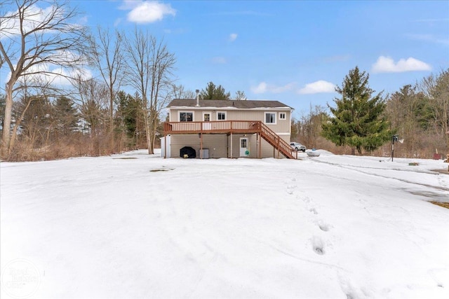 snow covered house featuring a garage, stairway, and a wooden deck