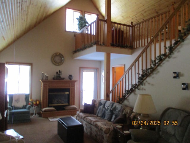 living area with stairs, plenty of natural light, a glass covered fireplace, and wooden ceiling