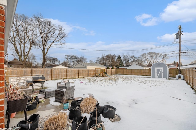 yard covered in snow with an outbuilding, a fenced backyard, a playground, and a storage shed