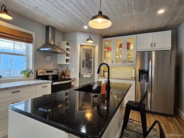 kitchen featuring a large island, glass insert cabinets, appliances with stainless steel finishes, wall chimney range hood, and pendant lighting