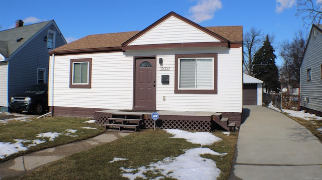 bungalow-style home with a yard, roof with shingles, a detached garage, and an outdoor structure