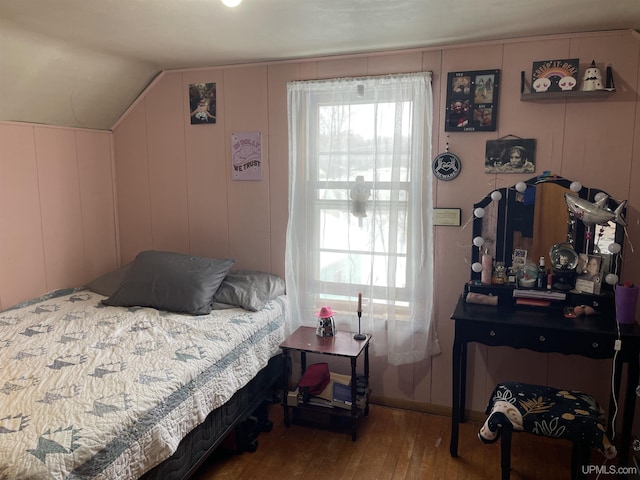 bedroom featuring multiple windows, vaulted ceiling, a decorative wall, and wood finished floors