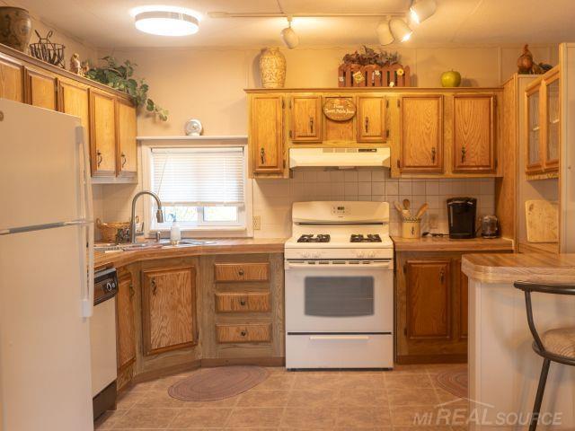 kitchen with white appliances, brown cabinetry, light countertops, under cabinet range hood, and a sink