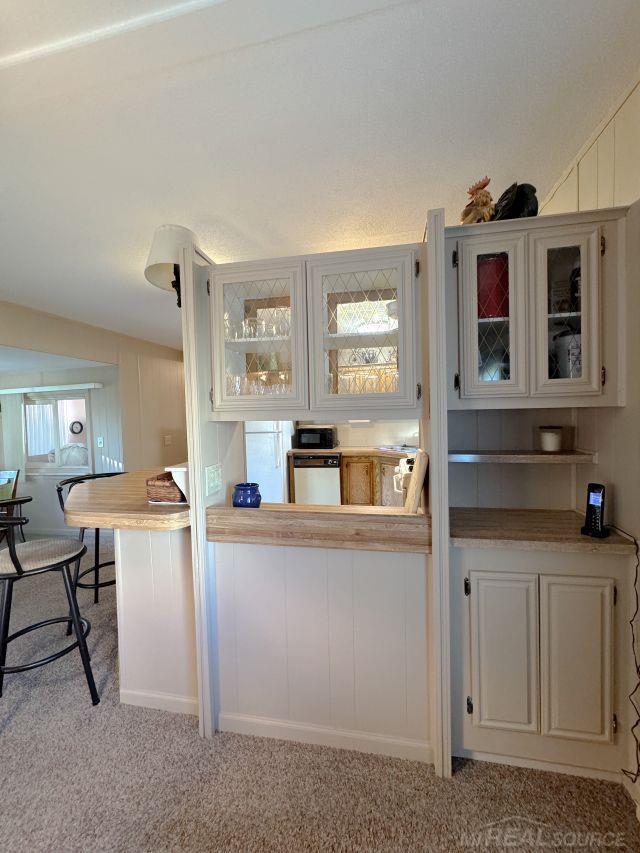 interior space featuring a breakfast bar, glass insert cabinets, light carpet, black microwave, and dishwasher