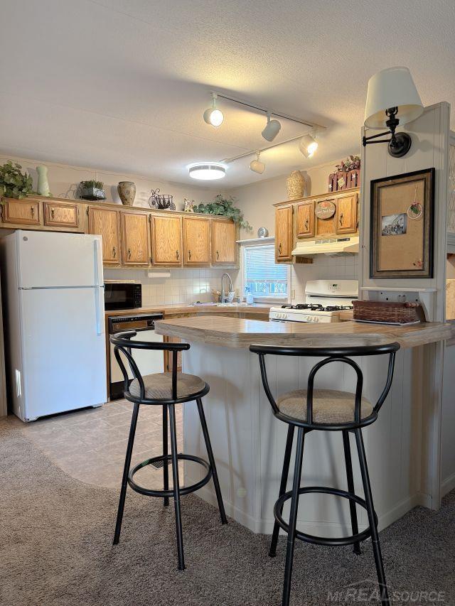 kitchen featuring white appliances, tasteful backsplash, a kitchen breakfast bar, under cabinet range hood, and a sink