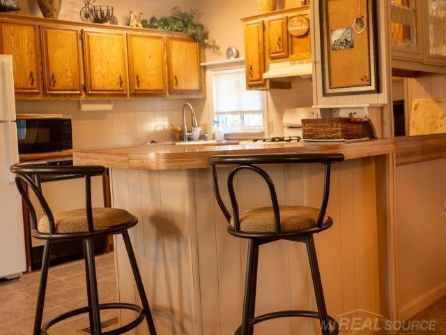 kitchen featuring brown cabinets, under cabinet range hood, black microwave, and a breakfast bar