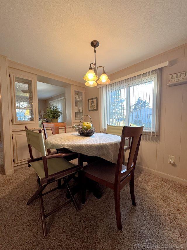 dining room with carpet floors, a notable chandelier, a decorative wall, and a textured ceiling