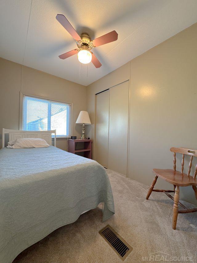 carpeted bedroom featuring a closet, visible vents, and a ceiling fan