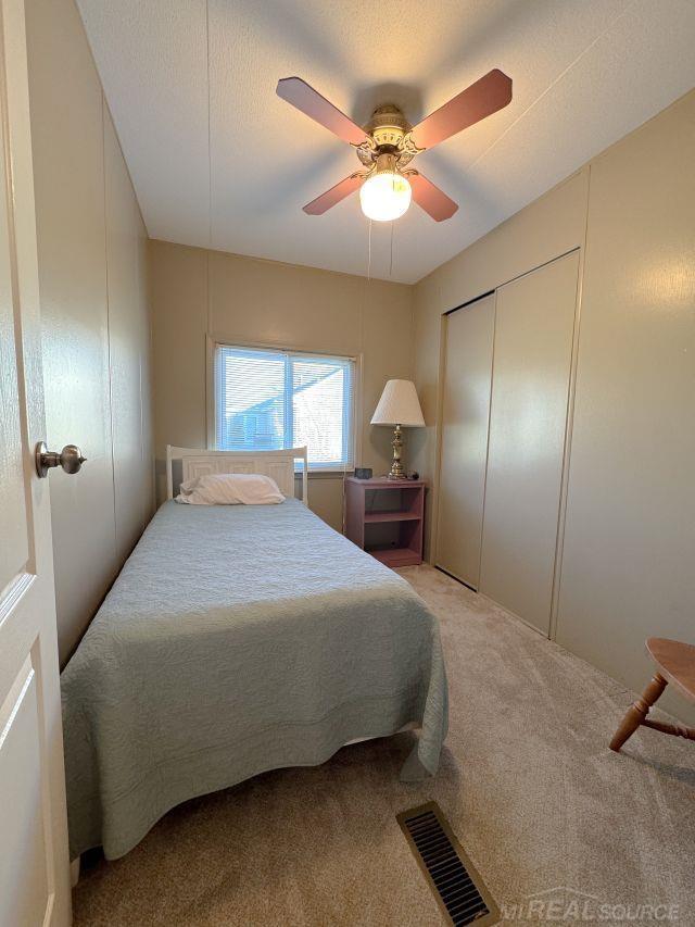 carpeted bedroom with ceiling fan, a textured ceiling, visible vents, and a closet