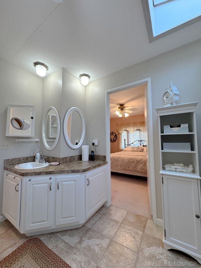 ensuite bathroom with a skylight, connected bathroom, vanity, and a textured ceiling