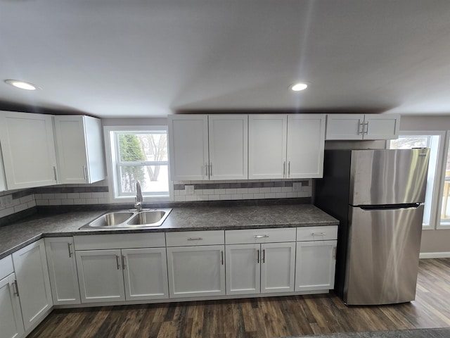 kitchen with dark countertops, a sink, freestanding refrigerator, and white cabinets