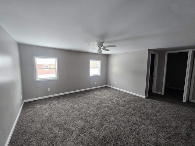 spare room with ceiling fan, dark colored carpet, and baseboards