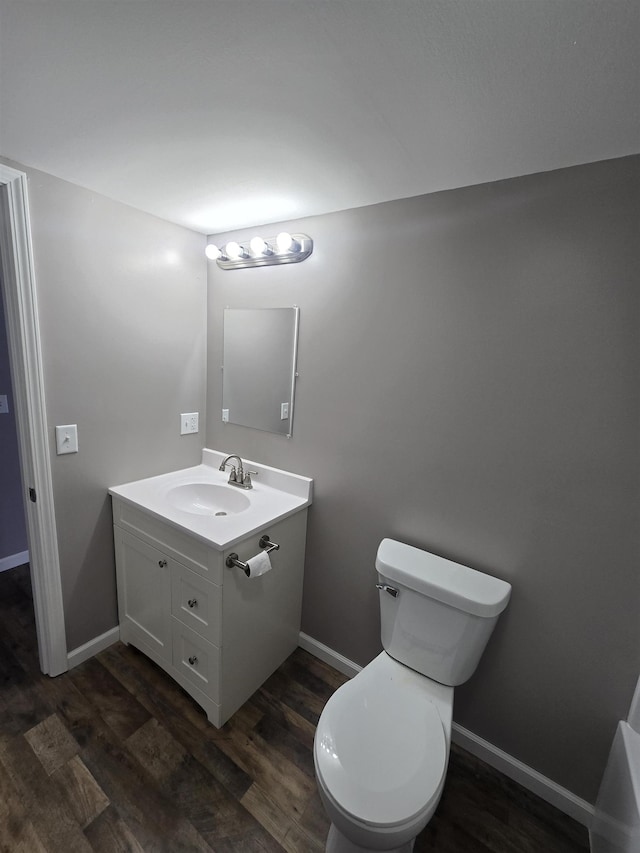 half bath with toilet, baseboards, wood finished floors, and vanity