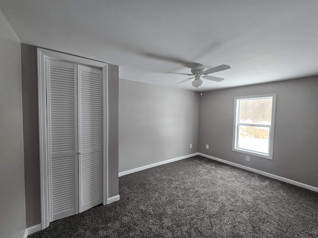 unfurnished bedroom featuring dark colored carpet, a closet, a ceiling fan, and baseboards