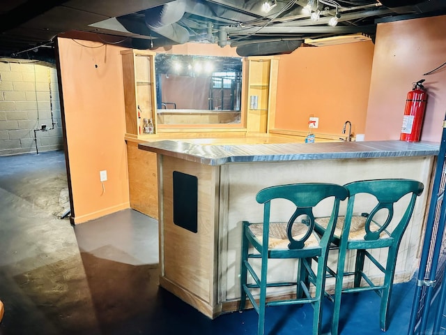 bar featuring concrete block wall, a sink, indoor bar, and concrete flooring