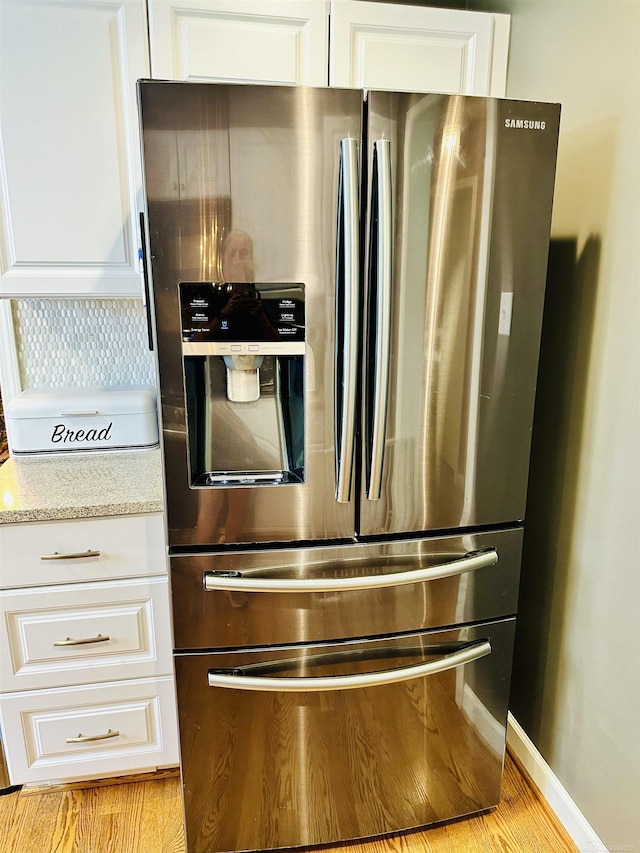 kitchen featuring light stone countertops, stainless steel fridge, and white cabinetry