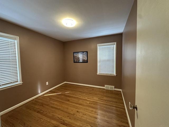 spare room with wood finished floors, visible vents, and baseboards