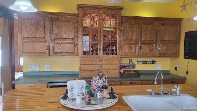 kitchen featuring dark countertops, glass insert cabinets, brown cabinets, and a sink