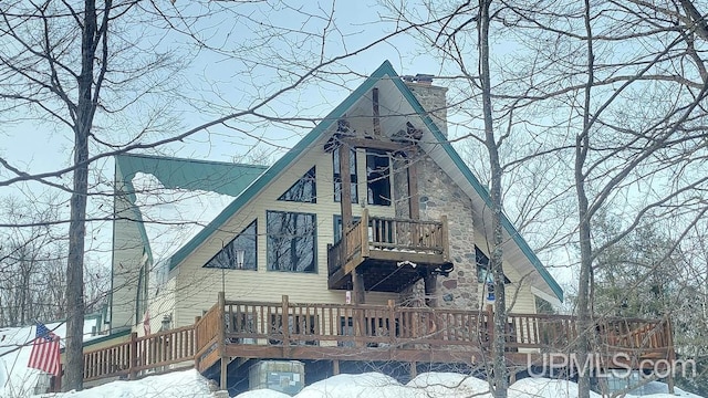 snow covered back of property featuring a chimney and a balcony