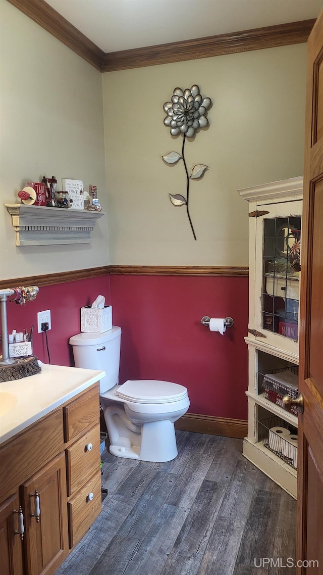 bathroom featuring baseboards, toilet, ornamental molding, wood finished floors, and vanity